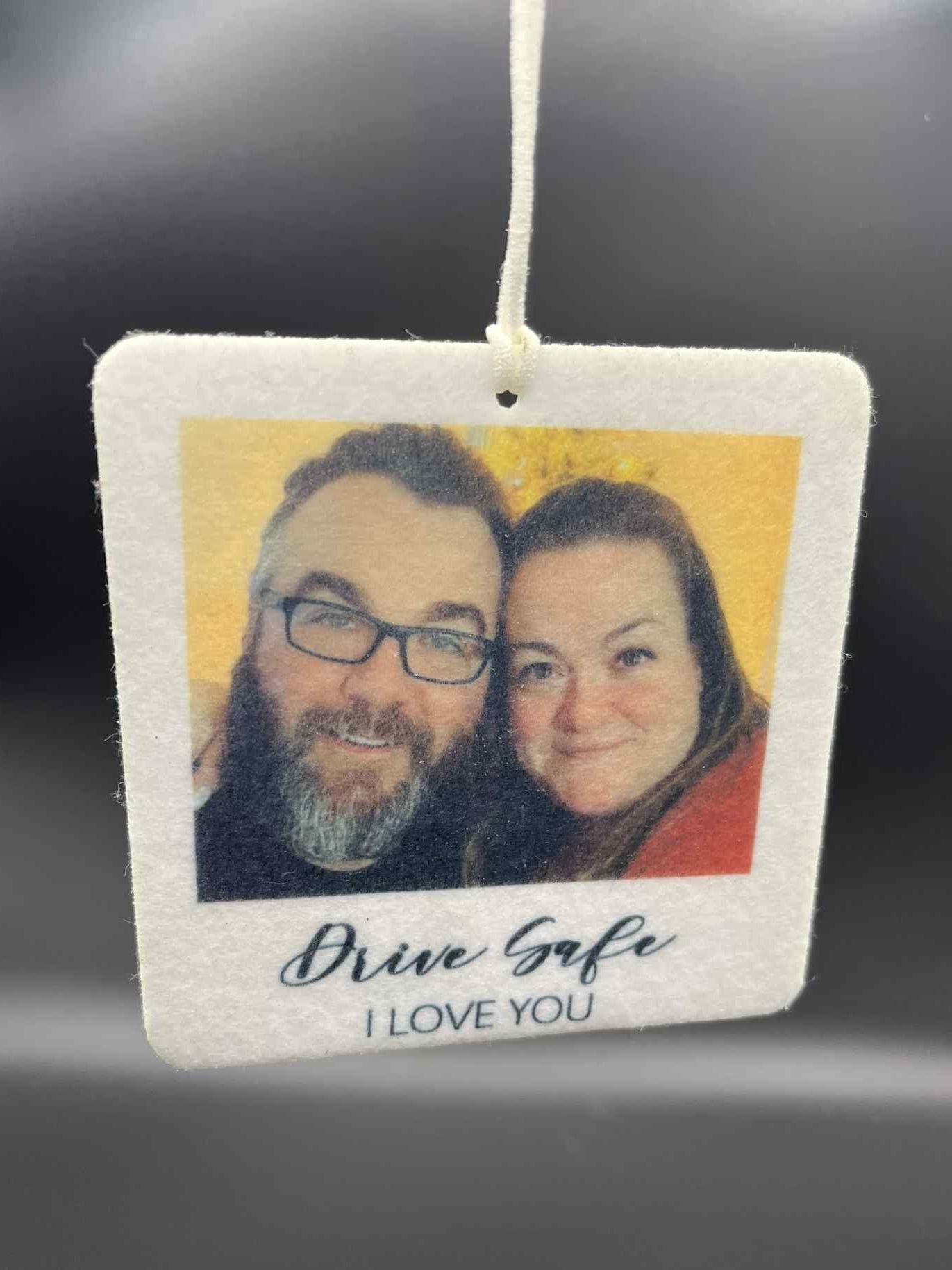 Car air freshener with a photo of two people and 'Drive Safe I Love You' text on a dark background.